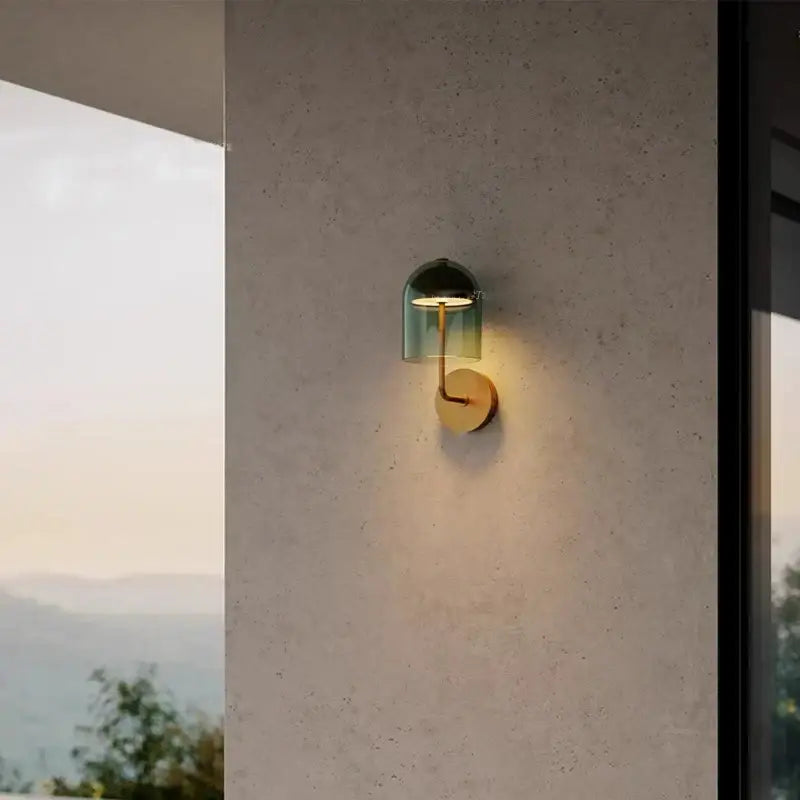 Modern wall sconce lamp with a translucent green glass dome and brass finish mounted on a circular base for bedrooms
