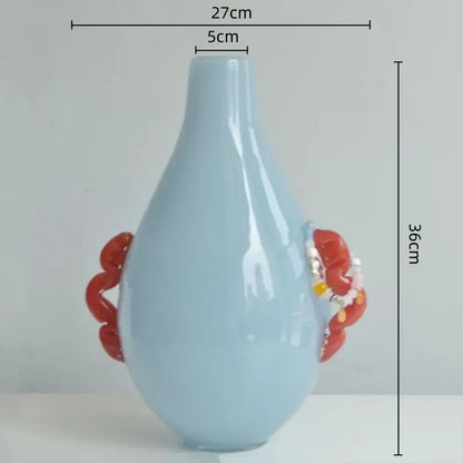 A light blue ceramic geometric flower vase with glossy finish and ornate red glass geometric handles for living room decor