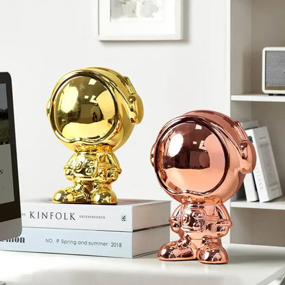 Two glossy metallic gold and rose gold decorbites astronaut statue spacemen on stacked books for living room decor