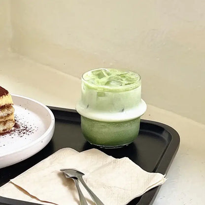 A layered green iced matcha drink in a clear modern borosilicate cap glass cup with ice and white rim for kitchen use