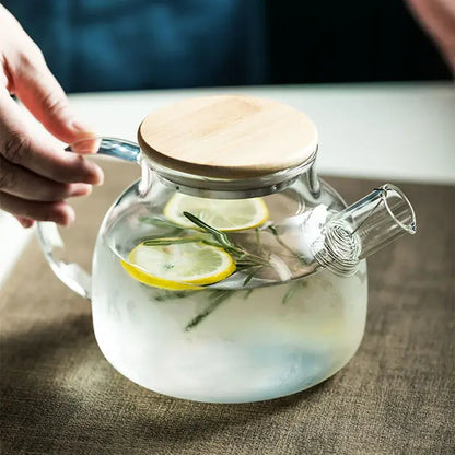 Modern borosilicate glass teapot with light wood handle filled with lemon slices and rosemary in transparent borosilicate glass