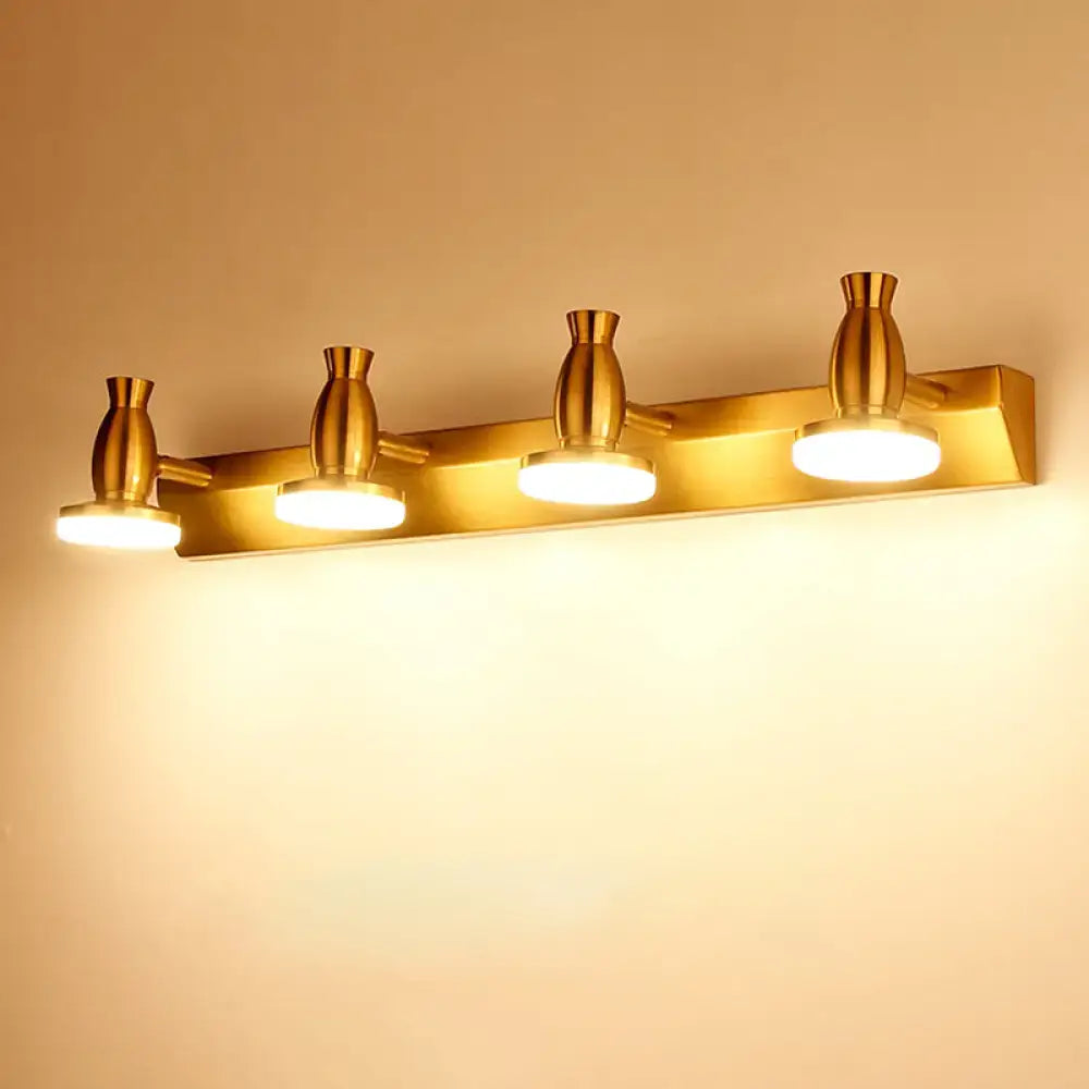 Modern brass bathroom vanity lamp with four gold-toned adjustable vase-shaped heads and round metal shade emitting warm light