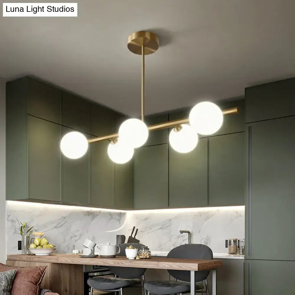Modern brass pendant light with five spherical glass shades arranged along a horizontal bar for dining room use