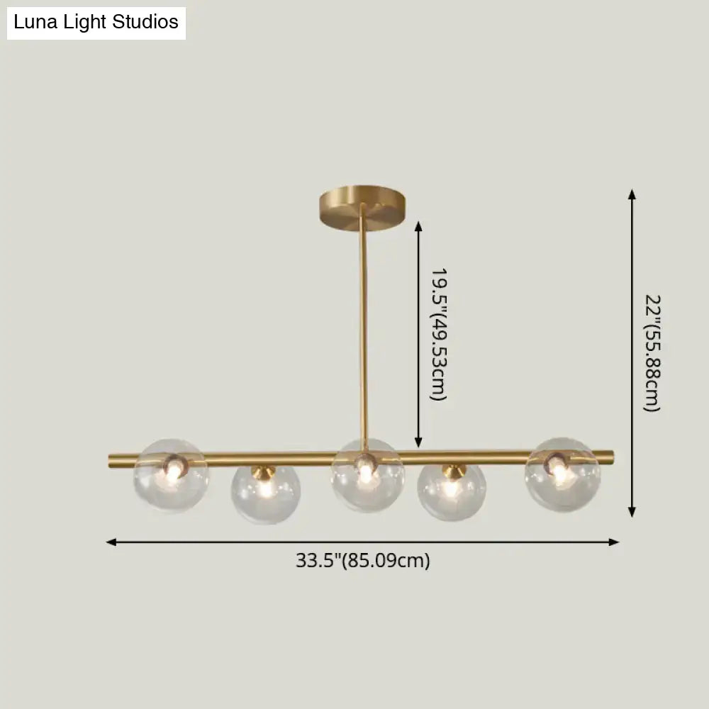 Modern brass 5-light pendant light with spherical glass shade and clear globes arranged horizontally for dining room