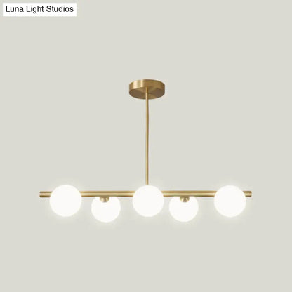 Modern brass pendant light with five spherical glass shade bulbs in a linear design for dining room lighting