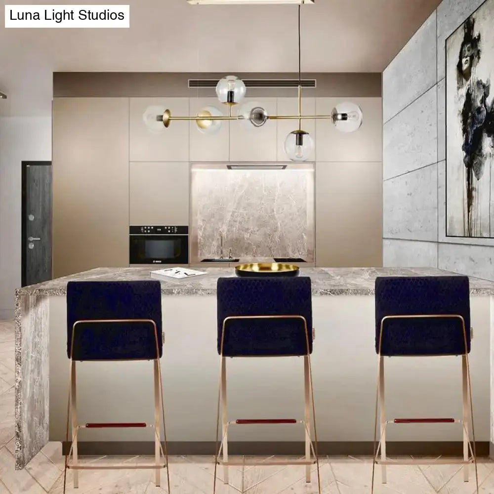 Three navy velvet bar stools with gold metal frames and red accent bars beside a modern brass 6-bulb island lamp with glass shade compatible with 110v-120v and 220v-240v