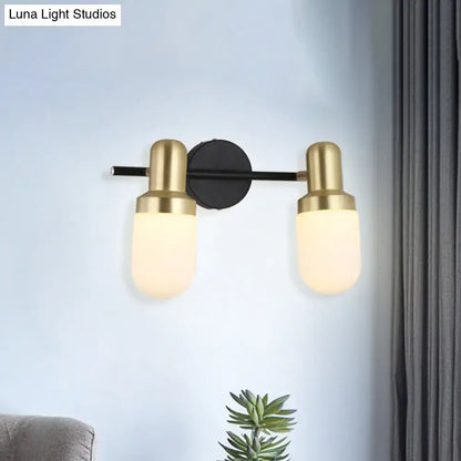 Modern brass and black glass sconce light with two brushed brass cylindrical shades and black circular mount for bedroom wall