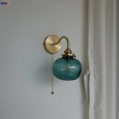 Modern brass wall sconce with a teal blue glass ball shade and exposed filament bulb with pull chain switch