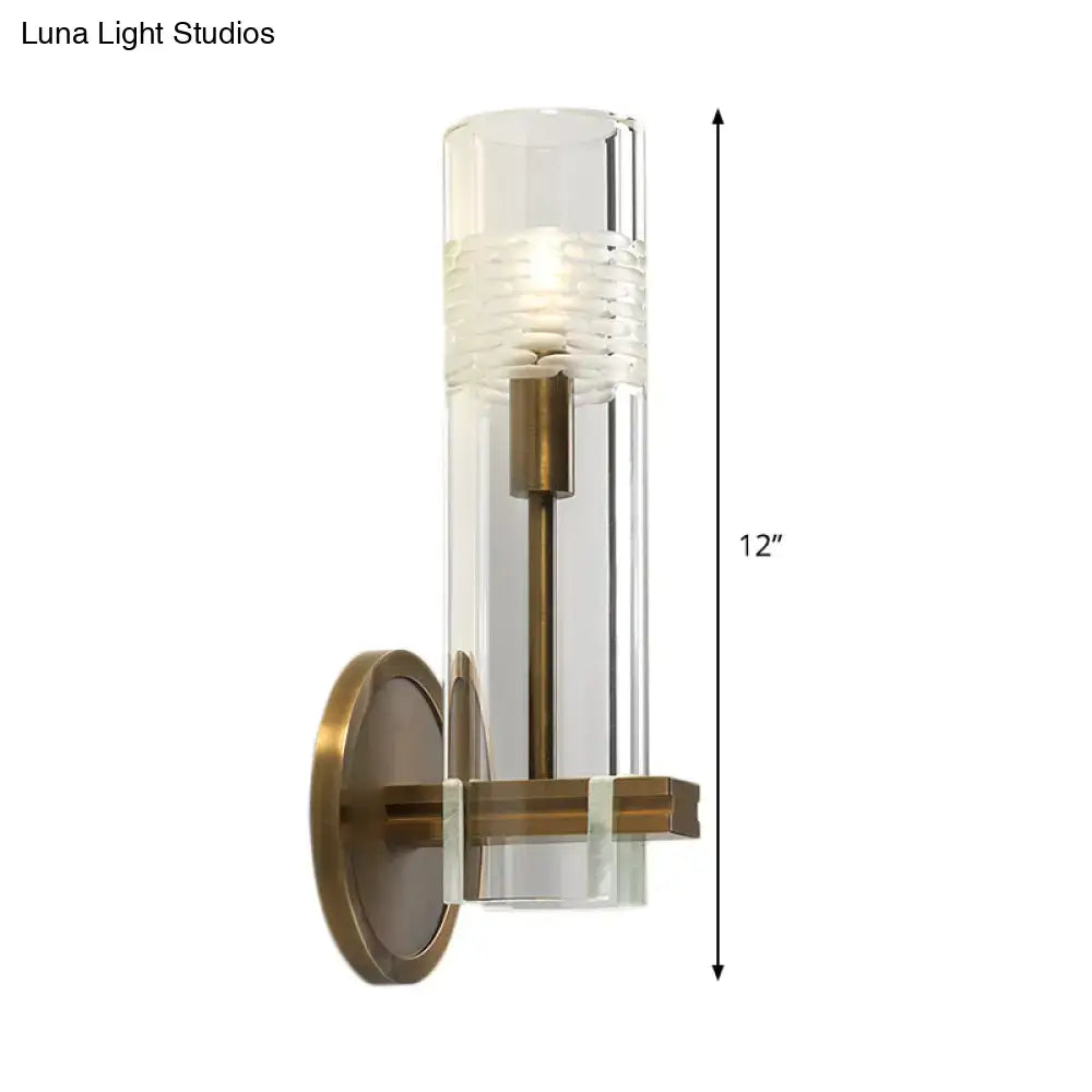 Modern brass and clear glass metal arm sconce with textured clear glass cylinder and antique brass base wall light