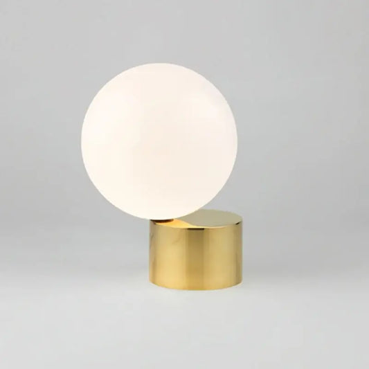 A modern brass and decorbites glass circular table lamp with a frosted white globe for bedroom use