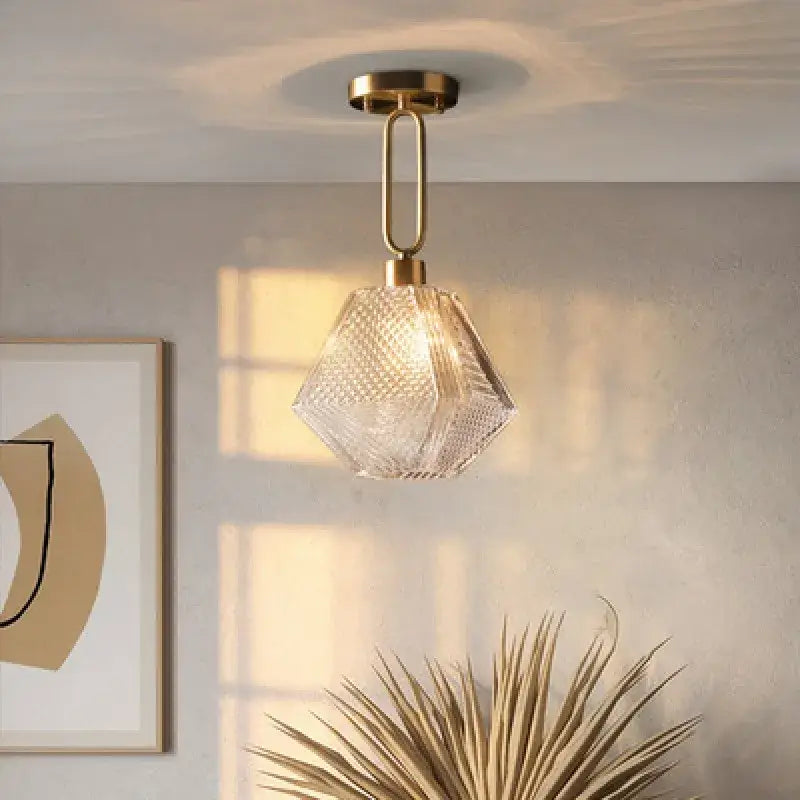 A clear faceted diamond glass pendant lamp with brass-finished metal fixture for modern living room lighting