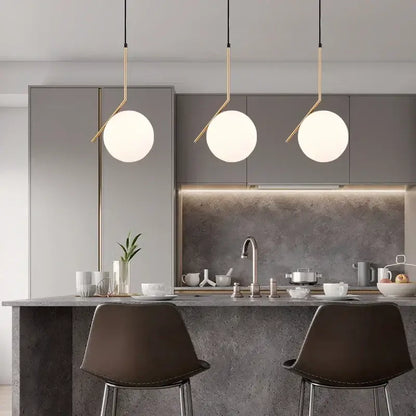 Three modern pendant lights with frosted glass ball shades and brass arms hang above a kitchen island decorbites light fixture