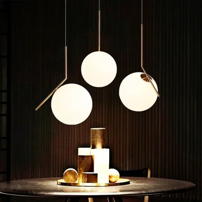 Three modern pendant lights with frosted glass ball shades and brass arms hang above a dark table decorbites light fixture