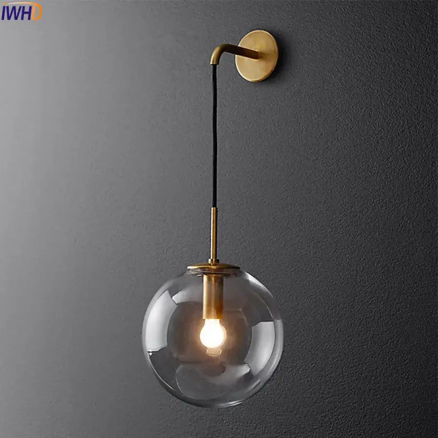 A modern brass wall lamp featuring a clear glass ball globe and black cord decorbites glass ball bathroom sconce