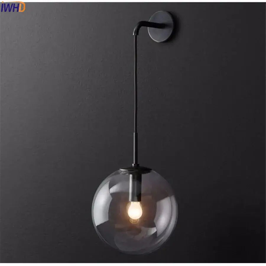 A sleek black metal wall lamp with a clear glass ball globe featuring an illuminated bulb by decorbites glass ball