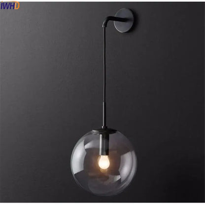 A sleek black metal wall lamp with a clear glass ball globe featuring an illuminated bulb by decorbites glass ball