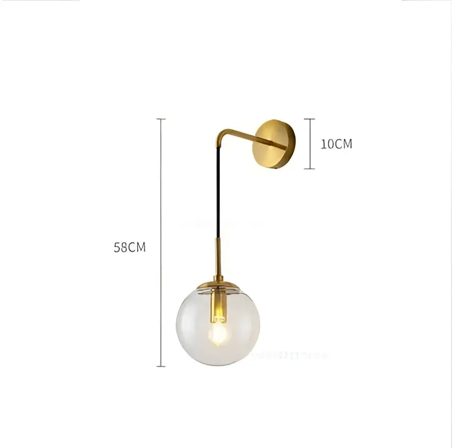 A sleek brass-finished wall lamp with a clear glass ball and exposed filament bulb for modern bedroom decorbites decor