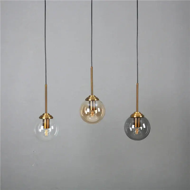 Three modern pendant lights with brass stems and clear amber and smoked gray glass pendant shades for kitchen dining room