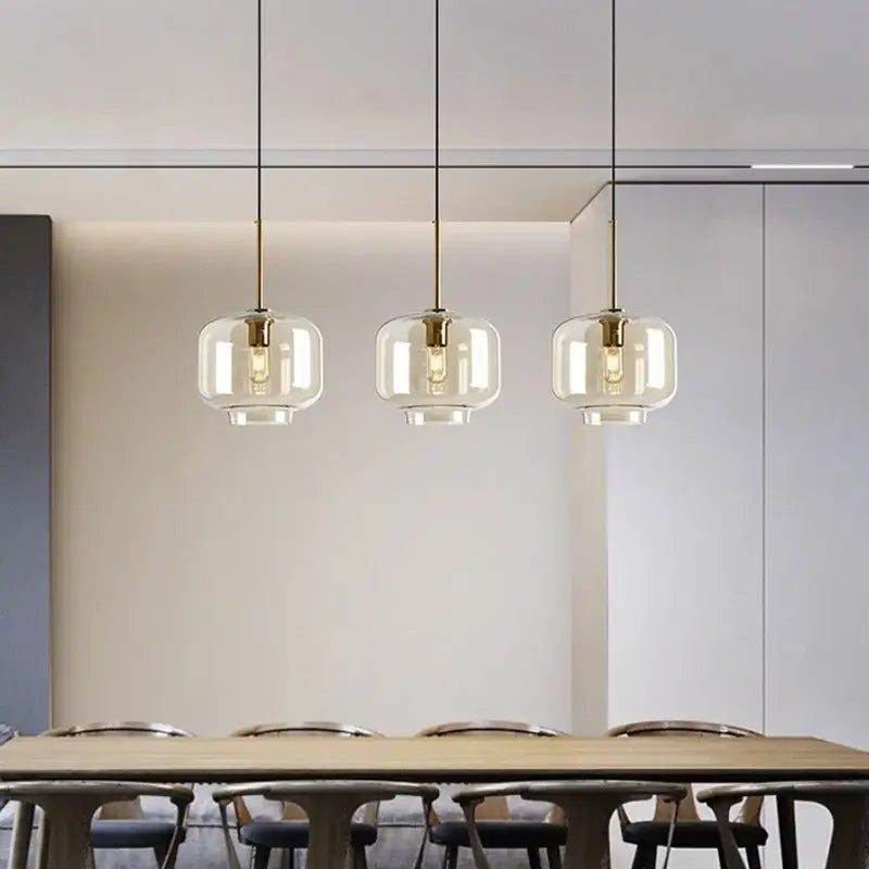 Modern brass and glass pendant lights with clear glass globes hanging above a dining table for kitchen use