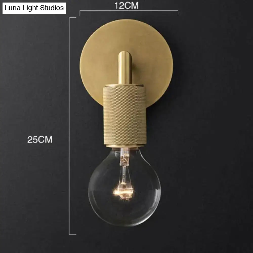 Modern brass and glass wall sconce with textured cylindrical middle section and exposed glass bulb for bedroom lighting