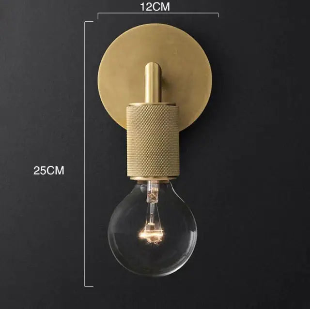 Modern brass and glass wall sconce with a textured cylindrical stem and an exposed bulb for bedroom lighting