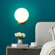 A sleek round wall mount lamp with frosted opal glass globe and brass base for bedroom bedside use