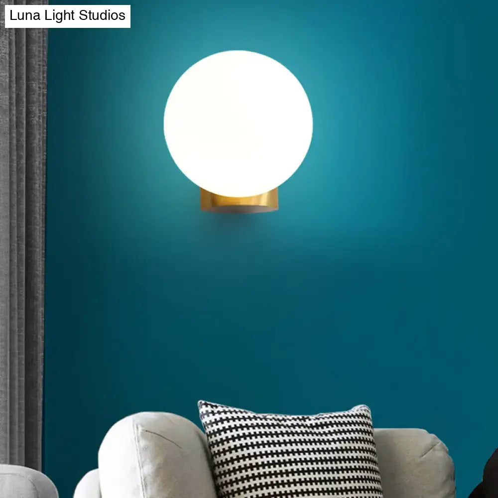 A sleek modern wall mount lamp with a frosted opal glass globe and polished brass base for bedside use
