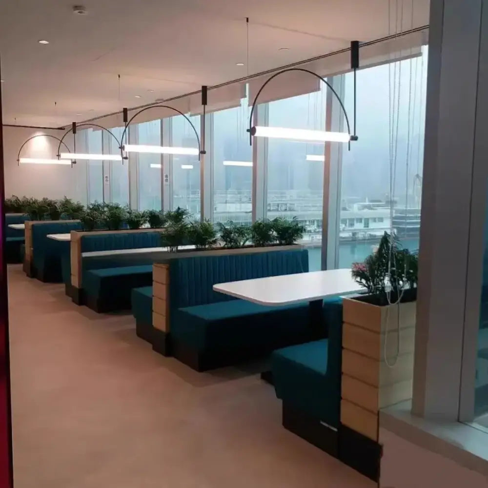 Teal upholstered booth seating with wooden panels and white tabletops under polished chrome pendant light bars