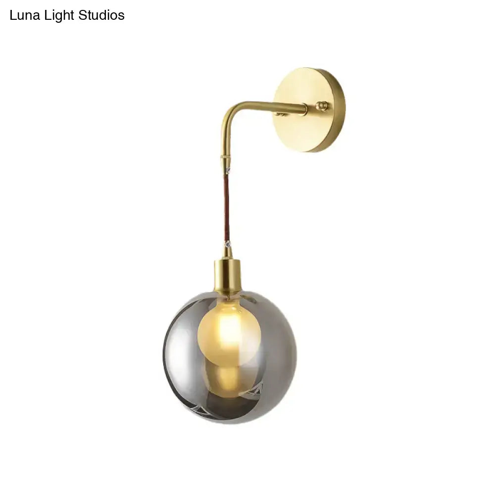 A modern brass and smoke gray glass corner wall light with a sleek finish and spherical shade for bedroom use