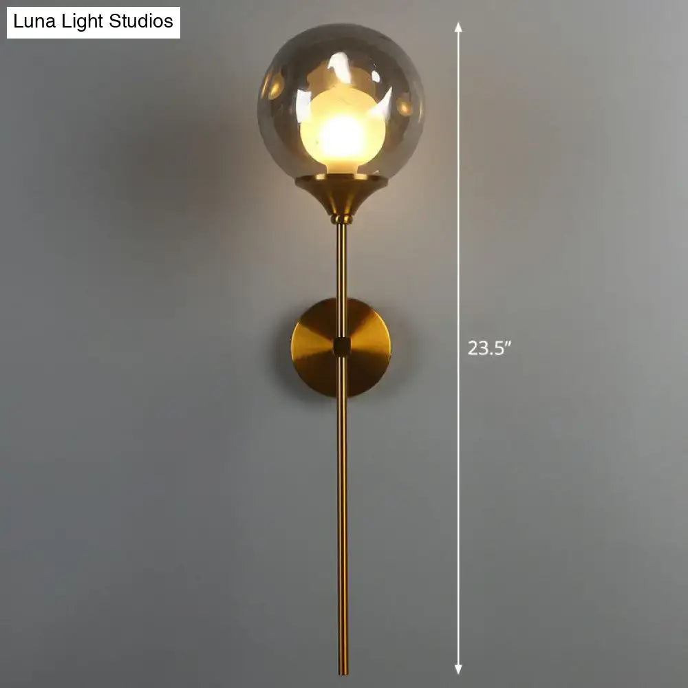 Modern brass wall light with smoke gray glass globe and slender stem ideal for bedroom sconce lighting
