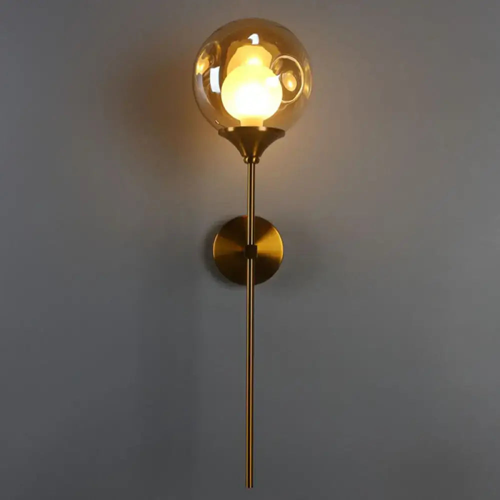 Modern brass and smoke gray glass wall light with gold-toned spherical globe, slender brass stem, and circular base for bedroom
