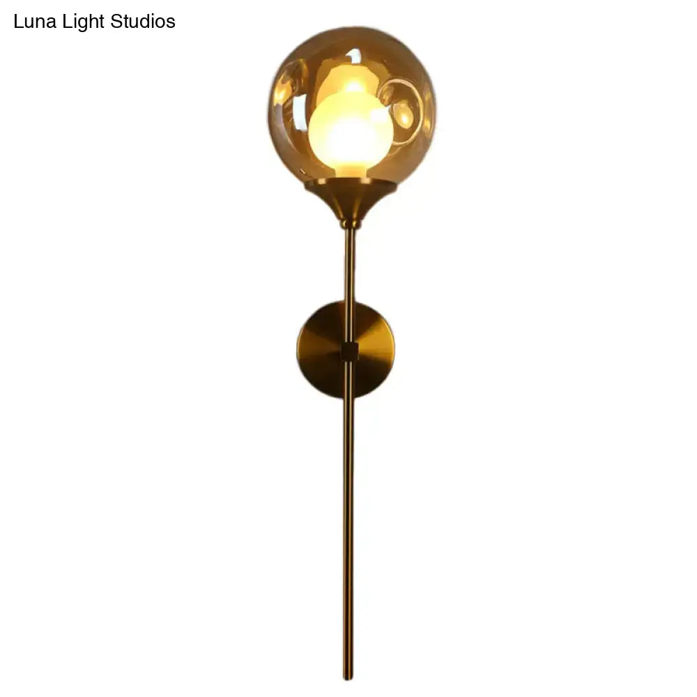 A modern brass wall light with smoke gray glass and an amber globe illuminating the bedroom sconce