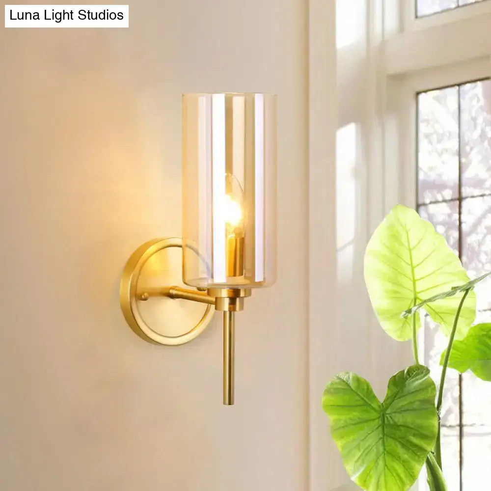 Modern brass wall sconce with gold-toned finish, cylindrical smoked glass shade, and e26 bulb base vertical ridges