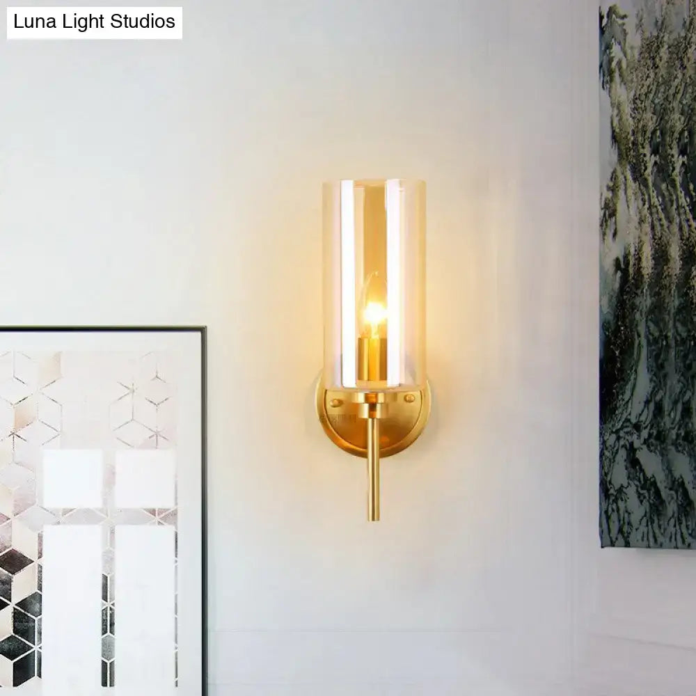 Modern brass wall sconce with a gold-toned finish and clear cylindrical glass shade with e26 bulb base