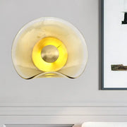 Modern brass and tan glass wall light fixture with amber curved glass and central brass accent for bedroom sconce use