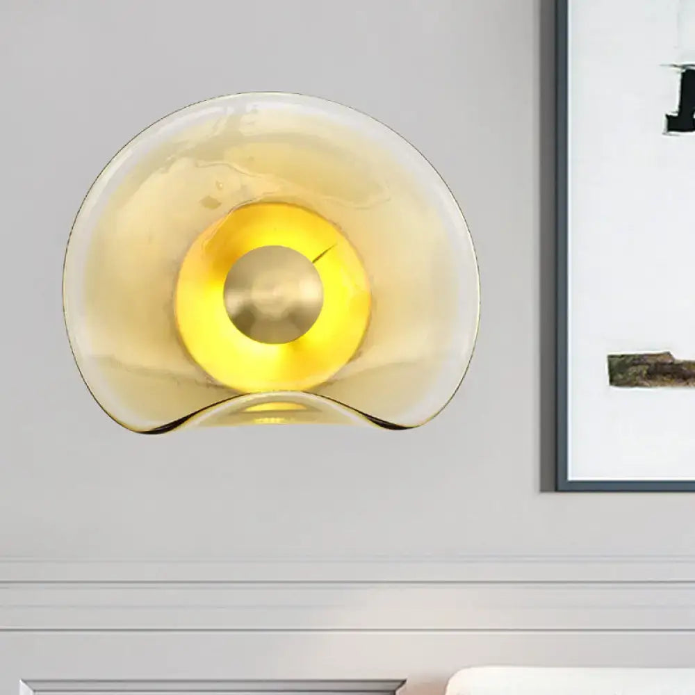 Modern brass and tan glass wall light fixture with amber curved glass and central brass accent for bedroom sconce use