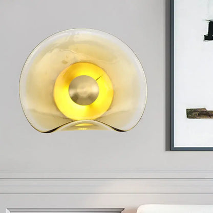 Modern brass and tan glass wall light fixture with amber curved glass and central brass accent for bedroom sconce use