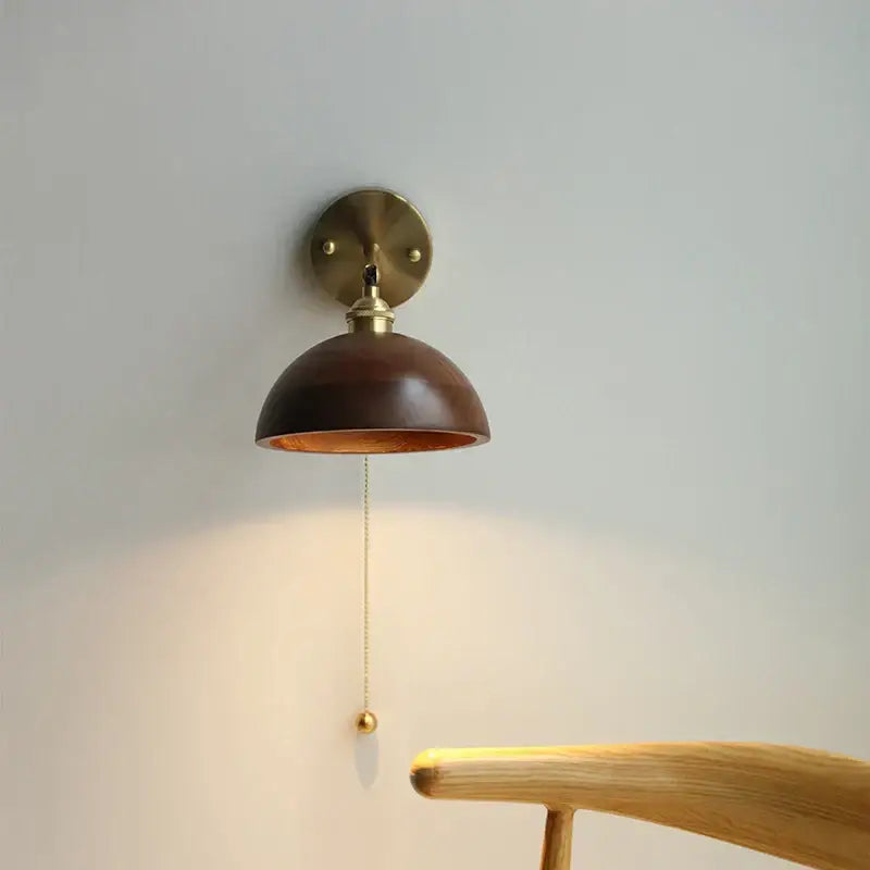 A warm-toned modern brass wall sconce with a polished dark wood dome shade and decorbites led walnut pull chain