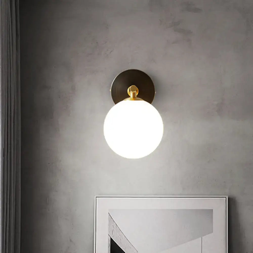 Modern brass and white glass wall sconce with gold-toned sphere, frosted white glass globe, and matte black backplate