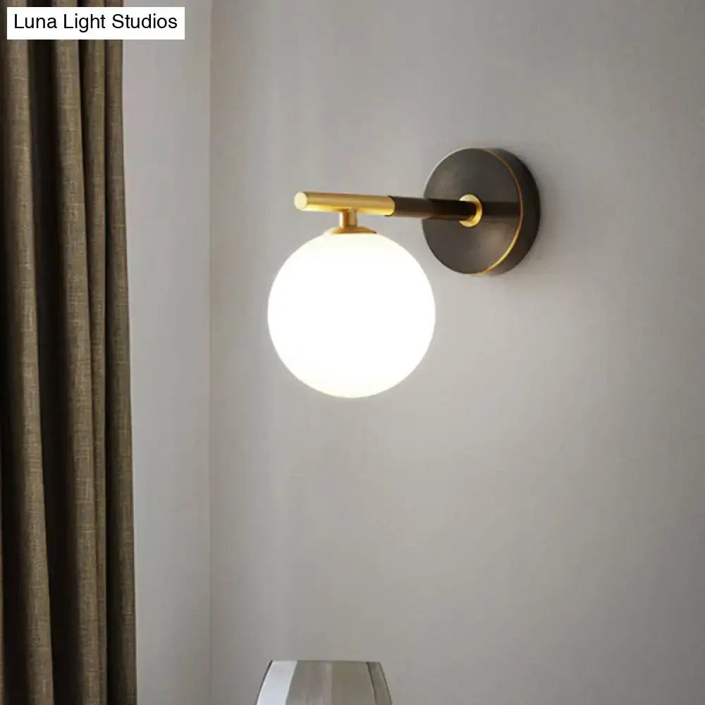 A modern brass and white glass wall sconce with matte black base and gold-toned arm for bedroom lighting