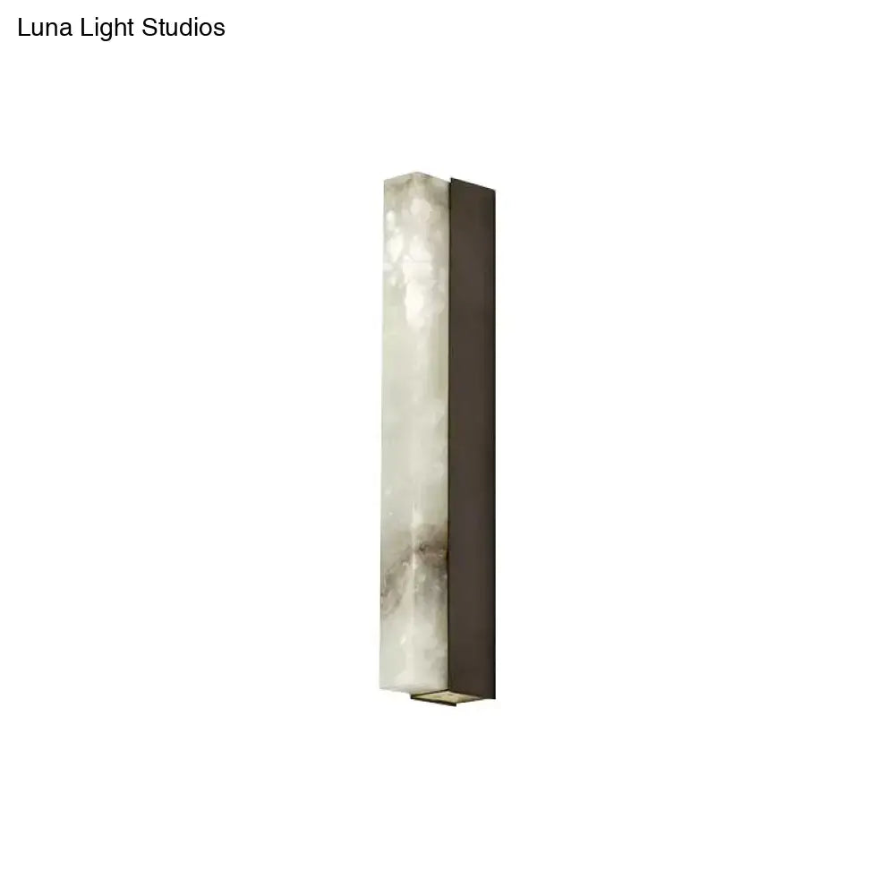 A modern brass and white onyx wall lighting sconce with natural veining in a dark bronze frame for living room use