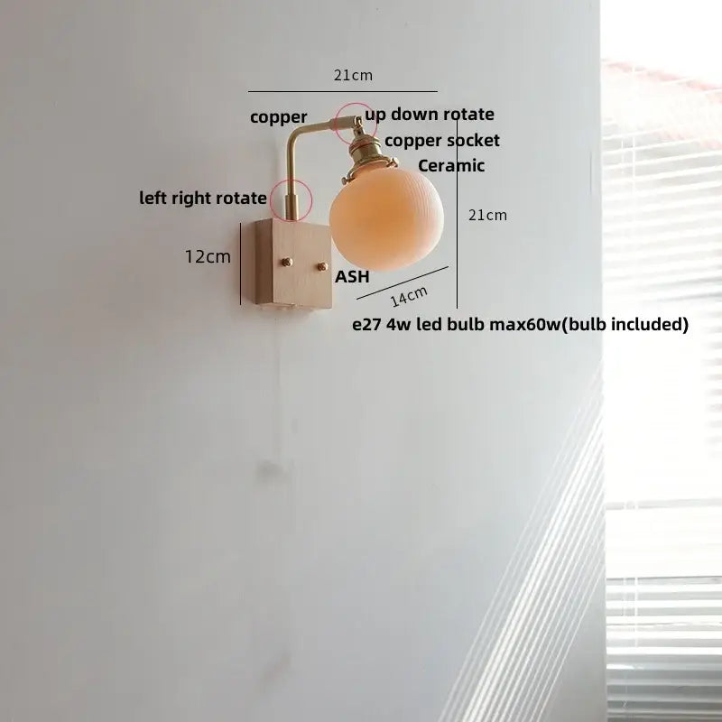 Copper-finished wall light fixture with matte ceramic globe shade and modern brass and wood elements for bedroom use