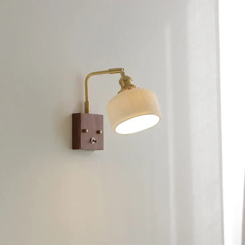 Modern brass and wood wall light fixture with a ribbed off-white glass shade mounted on a dark wood base