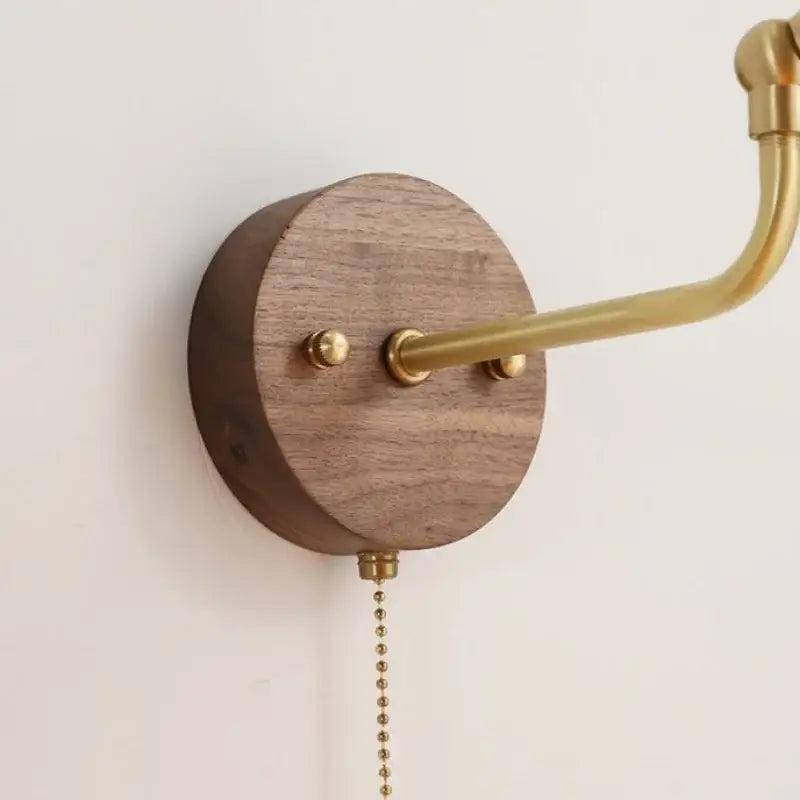 Modern brass and wood wall sconce with a round walnut base, curved arm, chain pull switch, and amber led light for bathroom decorbites copper glass style