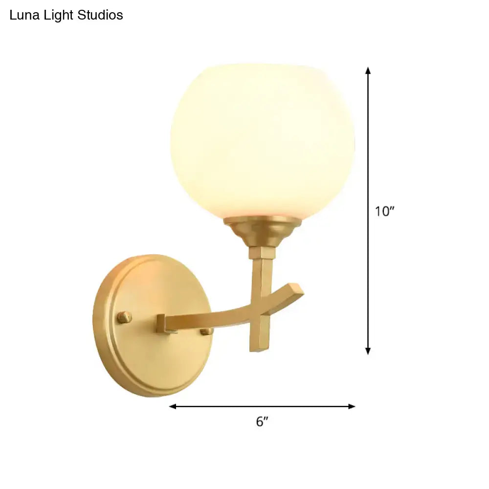 Modern brass armed wall sconce with gold finish and frosted opal glass shade for bedroom lighting