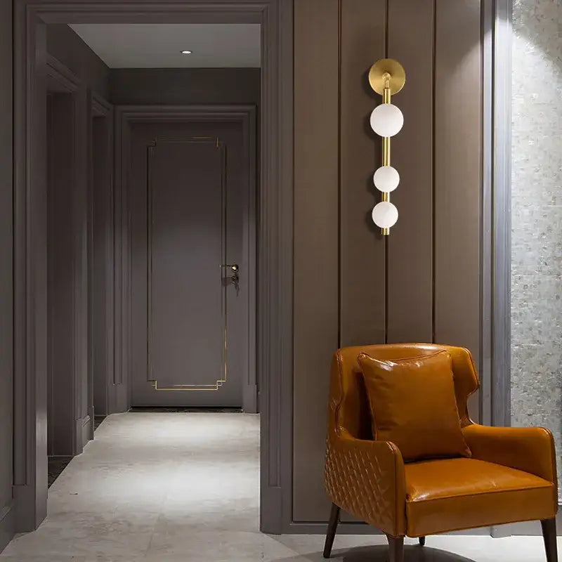 A modern brass and black frosted glass wall lamp paired with a rich tan leather armchair for elegant mirror headlight decorbites