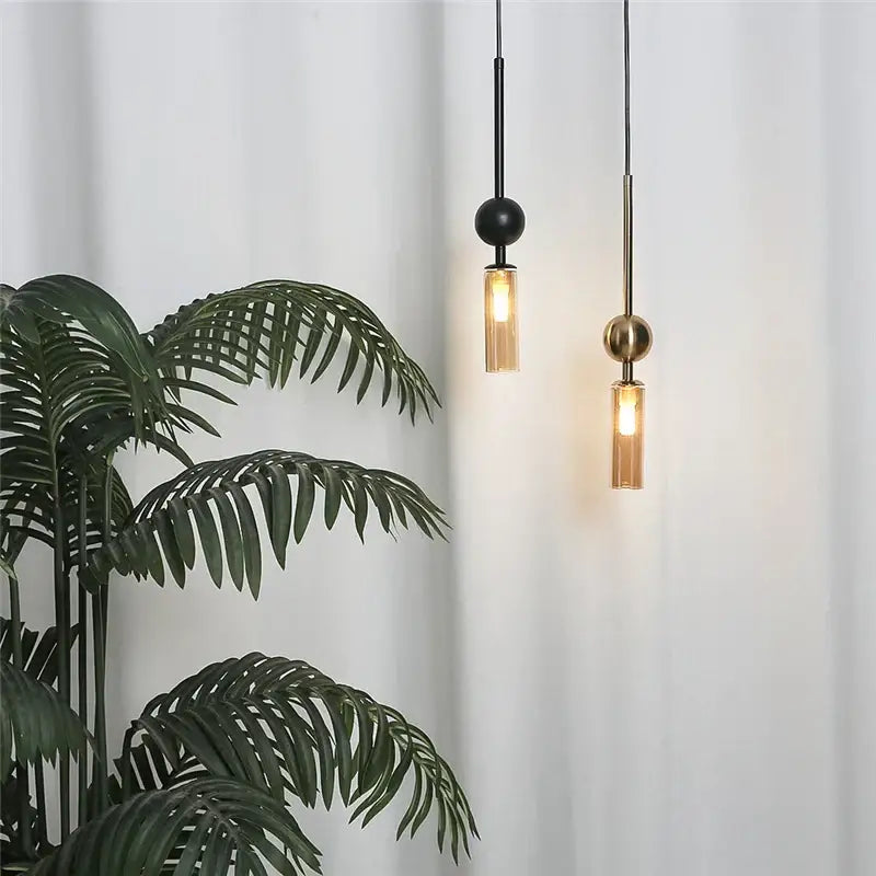 Two modern brass and black glass pendant lights with spherical tops and cylindrical shades featuring led bulb design style