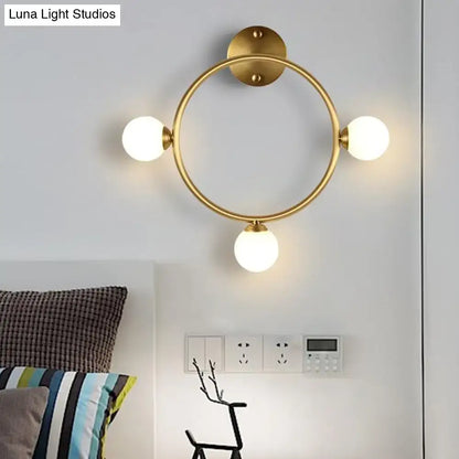 Modern brass circular wall light fixture with gold-toned finish and three frosted glass globe bulbs for bedroom use