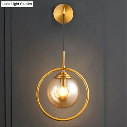 Modern brass circular wall mounted lamp with gold-toned spherical pendant and clear glass globe shade for bedroom
