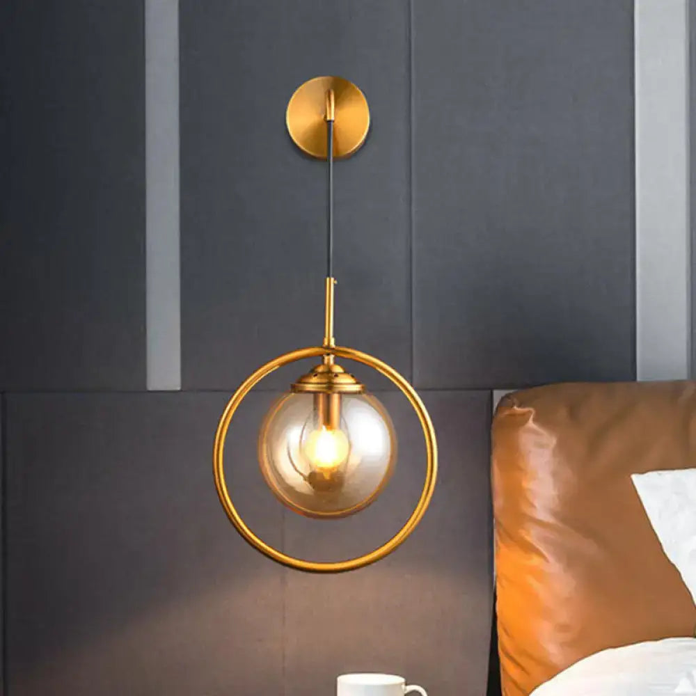 Modern brass circular wall mounted lamp with gold-toned frame and clear glass globe housing an exposed bulb